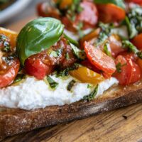 Bruschetta with roasted tomatoes, basil, and burrata on a rustic wooden board